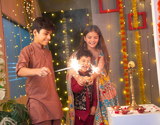 Low angle view of cheerful siblings in traditional attires playing with sparklers while celebrating Diwali at home